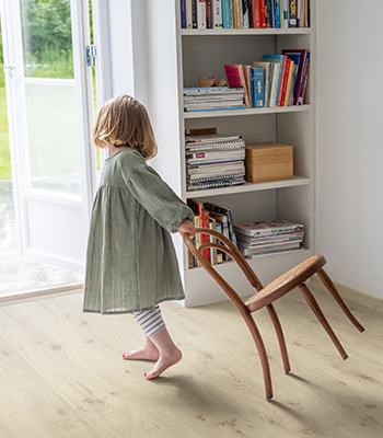 Kind zieht Stuhl über beigefarbenen Laminatfussboden